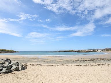 A sandy beach with rocks and calm sea under a partly cloudy sky at Little Mead in Trearddur Bay