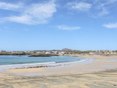 A sandy beach with gentle waves and houses in the distance at Little Mead in Trearddur Bay