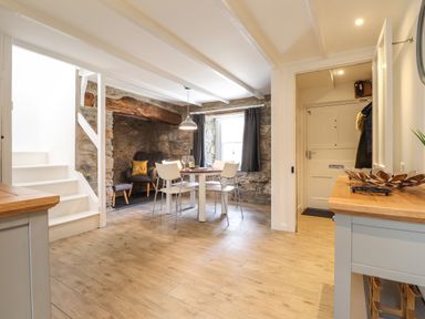 A dining area with a round table and white chairs next to a stone wall with a built-in seating area and stairs in Awelfa Newport Pembrokeshire