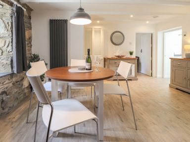 A dining area with a round table set with a bottle and glasses surrounded by four chairs at Awelfa in Newport Pembrokeshire