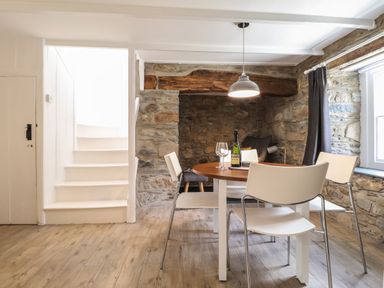 A dining area with a round table and white chairs next to a stone wall and white stairs at Awelfa Newport Pembrokeshire
