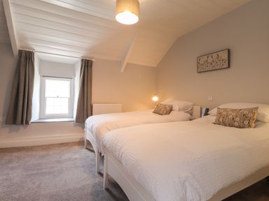 A bedroom with two single beds white bedding a window with curtains and a ceiling light at Awelfa in Newport Pembrokeshire