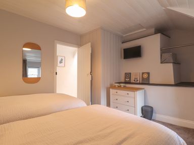 A bedroom with two beds a wall mirror a chest of drawers and a small wall-mounted television at Awelfa in Newport Pembrokeshire