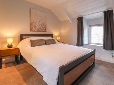 A bedroom with a bed a white bedspread two bedside tables with lamps a window with curtains and a painting above the bed at Awelfa Newport Pembrokeshire