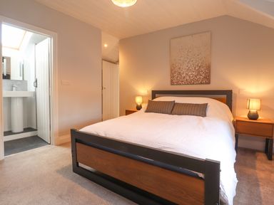 A bedroom with a double bed between two bedside tables with lamps and a bathroom visible at Awelfa in Newport Pembrokeshire