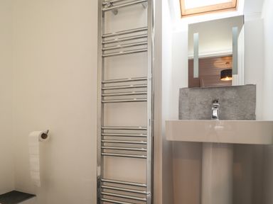 A bathroom with a pedestal sink a metal towel rack a mirror and a toilet paper holder at Awelfa in Newport Pembrokeshire