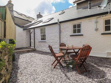 An outdoor patio area with a round wooden table and four wooden chairs on a gravel surface at Awelfa in Newport Pembrokeshire
