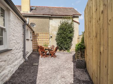 An outdoor patio area with a wooden table and four chairs next to a building with a white stone wall at Awelfa in Newport Pembrokeshire