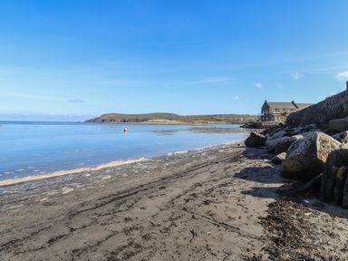 A sandy beach with rocks and a stone building near the shoreline at Awelfa in Newport Pembrokeshire