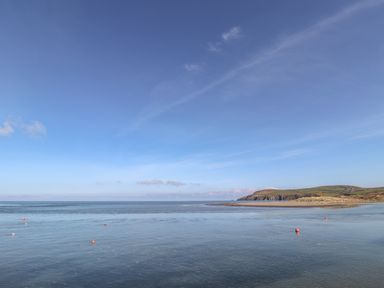 A coastal scene with calm water buoys and a sandy beach with hills in the distance at Awelfa in Newport Pembrokeshire