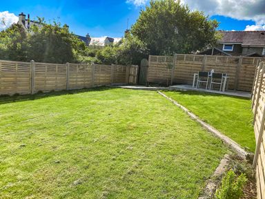 A fenced garden with a grassy lawn and a patio table with chairs at Awelfa in Newport Pembrokeshire