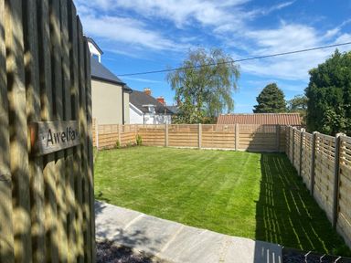 A fenced grassy backyard with a tree a shed and houses in the background at Awelfa in Newport Pembrokeshire