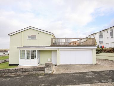 A two-story house with a garage and a wooden balcony with a picnic table at The Little Dolphins in Rhosneigr