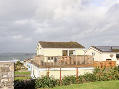 A house with a wooden deck overlooking the sea at The Little Dolphins in Rhosneigr