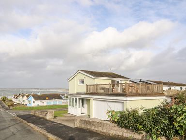 A two story house with a wooden balcony overlooking the sea and a row of smaller houses nearby at The Little Dolphins in Rhosneigr