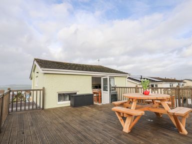 A large wooden deck with a round wooden picnic table and a small green plant on it at The Little Dolphins in Rhosneigr