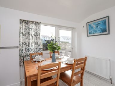 A dining room with wooden table and chairs set with plates glasses and a vase with flowers at The Little Dolphins in Rhosneigr