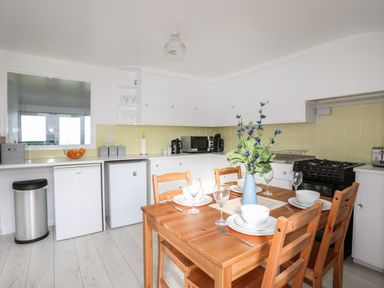 A kitchen with a wooden dining table set for four and white cabinets at The Little Dolphins in Rhosneigr