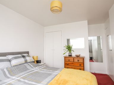 A bedroom with a bed gray yellow bedding wooden chest of drawers and a plant at The Little Dolphins in Rhosneigr