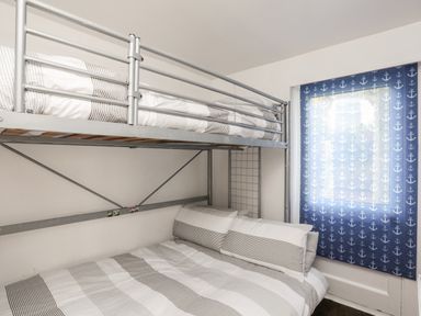 A bedroom with a bunk bed and striped bedding next to a window with blue anchor patterned curtains at The Little Dolphins in Rhosneigr