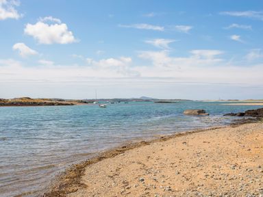 A sandy beach with rocks and boats on the water under a partly cloudy sky at The Little Dolphins in Rhosneigr
