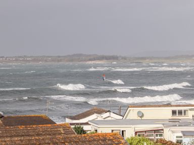 A view of a coastal area with houses in the foreground and a person windsurfing in the sea at The Little Dolphins in Rhosneigr
