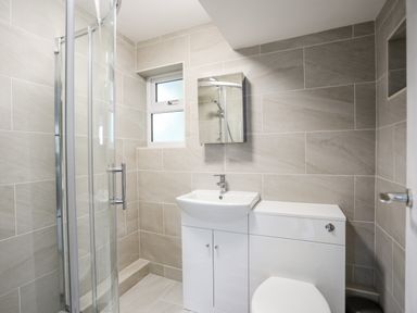 A bathroom with a shower enclosure a sink with cabinet a mirror and a toilet at The Little Dolphins in Rhosneigr