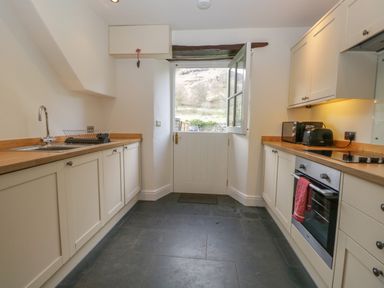 A kitchen with cream cabinets a wooden countertop a sink an oven and a door with a window at Oak Tree Cottage in Coniston