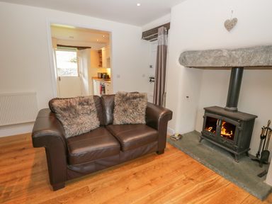 A living room with a leather sofa with two fur cushions and a wood burning stove at Oak Tree Cottage in Coniston