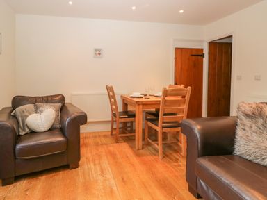 A room with two brown leather armchairs and a wooden dining table with four chairs at Oak Tree Cottage in Coniston
