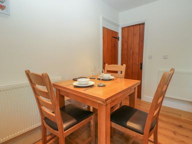A dining area with a wooden table set for four and four wooden chairs at Oak Tree Cottage in Coniston