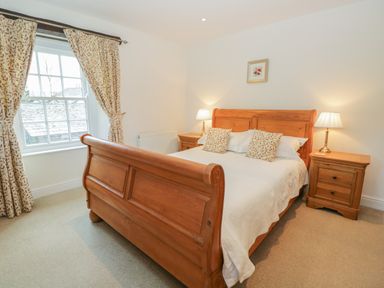A bedroom with a wooden bed white bedding patterned curtains and two bedside tables with lamps at Oak Tree Cottage in Coniston