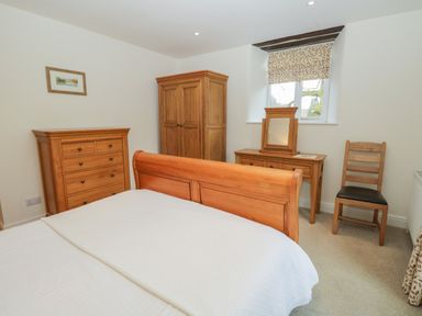 A bedroom with a wooden bed chest of drawers wardrobe dressing table and chair at Oak Tree Cottage in Coniston