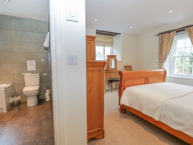A bedroom with a wooden bed and dressing table next to a bathroom with a toilet at Oak Tree Cottage in Coniston