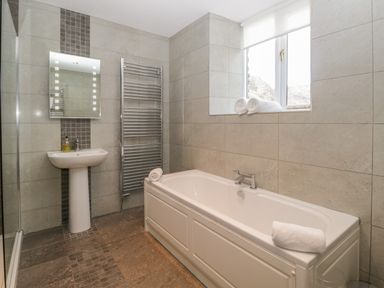 A bathroom with a bathtub towels a sink a mirror a heated towel rail and a window at Oak Tree Cottage in Coniston