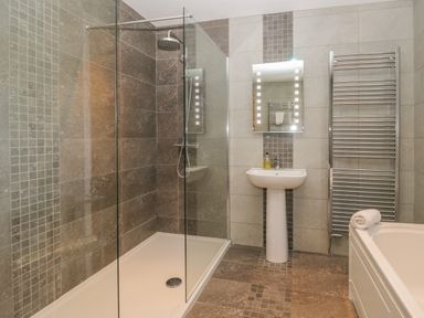 A bathroom with a walk-in shower, pedestal sink, lighted mirror, towel radiator, and bathtub at Oak Tree Cottage in Coniston