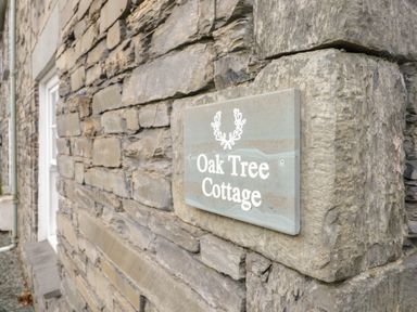 A stone wall with a sign that reads Oak Tree Cottage at Oak Tree Cottage in Coniston