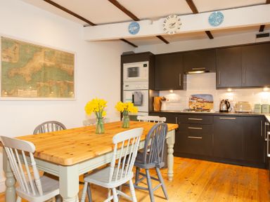 A kitchen with dark cabinets a wooden dining table with chairs and yellow flowers at The Sail Loft in St Ives