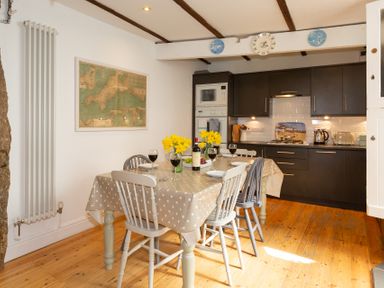 A kitchen with a dining table set with wine glasses and flowers at The Sail Loft in St Ives
