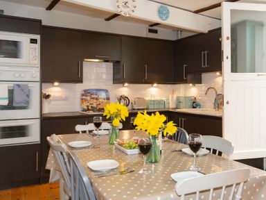 A kitchen with a dining table set with wine glasses and flowers at The Sail Loft in St Ives