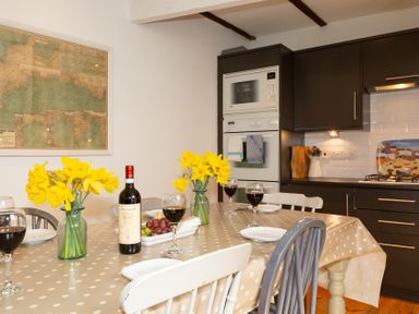 A kitchen with a dining table set with wine glasses, a bottle of wine, flowers, and plates at The Sail Loft in St Ives