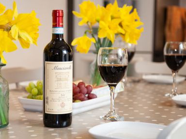 A dining table with a bottle of red wine glasses with wine yellow flowers and plates at The Sail Loft in St Ives