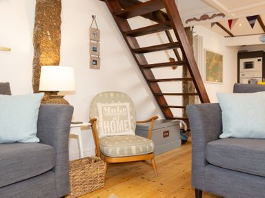 A seating area with two gray armchairs and a wooden chair with a cushion under wooden stairs at The Sail Loft in St Ives