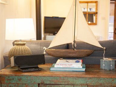 A living room table with books a model sailboat a lamp and a speaker at The Sail Loft in St Ives