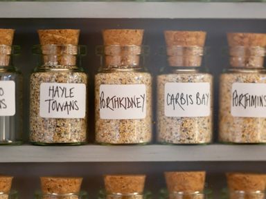 Glass jars with cork lids filled with sand labeled Hayle Towans Porthkidney Carbis Bay and Porthminster at The Sail Loft in St Ives