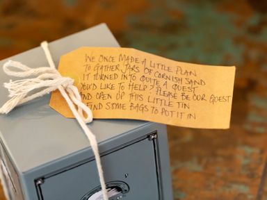 A gray tin box tied with white string and a handwritten note attached on a surface at The Sail Loft in St Ives