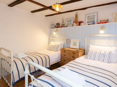 A bedroom with two single beds striped blankets wooden chest of drawers and decorated shelf at The Sail Loft in St Ives