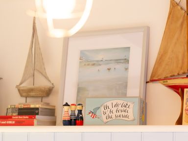 A shelf with model sailboats small figurines stacked books and a framed seaside painting at The Sail Loft in St Ives