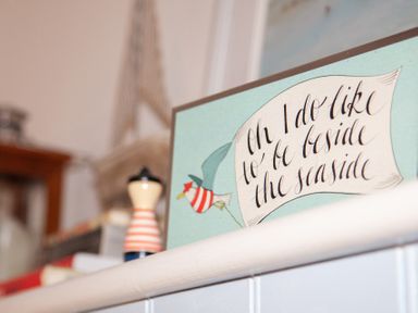 A decorative sign with a bird and text beside a small striped figure on a shelf at The Sail Loft in St Ives