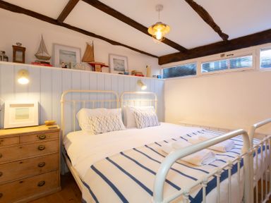 A bedroom with a double bed wooden chest of drawers and decorative model boats on shelf at The Sail Loft in St Ives